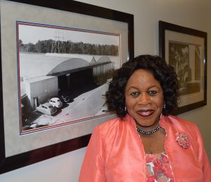 Shirley Kelly stands in front of a picture of the building she worked in when she started with the College of Engineering in 1967. They called it “the Hanger.”