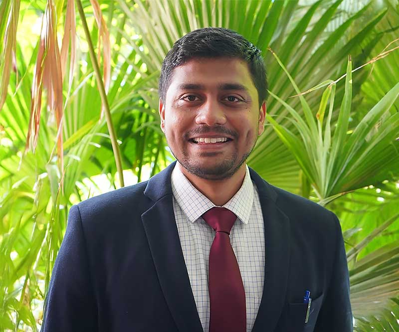 Shubham Ravan smiling outdoors in front of greenery.